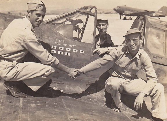 Maj Roland M Wilcox, on May 15, 1943, taken in Kunming China, serving with the 23rd Fighter Group, 75th Fighter Squadron of the Flying Tigers. That morning he had shot down 3 confirmed and 2 probable enemy aircraft in his P-40E. Pictured with Lt Col Bruce K Holloway, his daschund Joe, who had one zeke and one bomber that day, and Lt Charles Crysler who also had three confirmed and one probable victories that day.